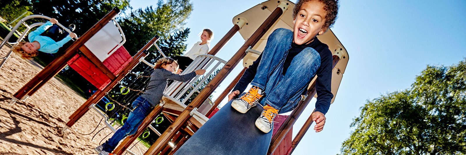 A young child squeels in delight as they slide off the play structure's fast pace glider